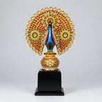 Front view of a stone-studded wooden peacock trophy with spread golden feathers, red and green embellishments and a black display base.