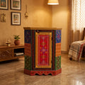 Traditional multicolour wooden corner cabinet displayed in a warm-toned room, featuring floral artwork and a curved decorative base