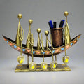 A tribal art metal pen holder with a boat design and a tribal man riding on it.