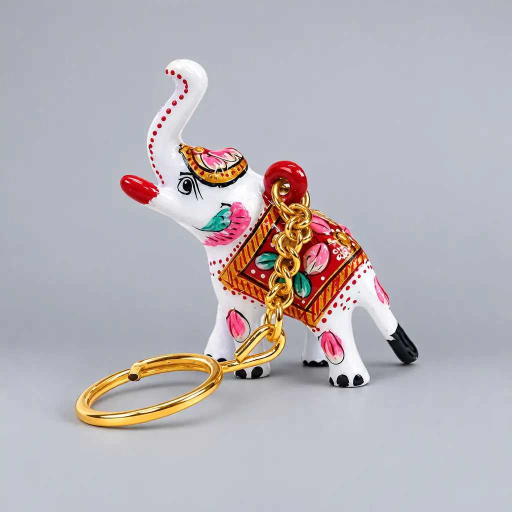 White elephant Meenakari keyring with pink and turquoise floral detailing, a red saddle and a gold-toned ring resting in front.
