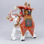 Front angled view of a white Meenakari Ambabari elephant with pink ear detailing, colourful floral patterns and riders under a red twin-domed canopy.