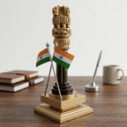 Wooden Ashoka Pillar memento with crossed Indian flags and a golden tiered base on a desk beside books and a mug