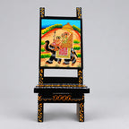 Front view of a wooden chair phone stand with an elephant procession painting and yellow detailing on a black frame.