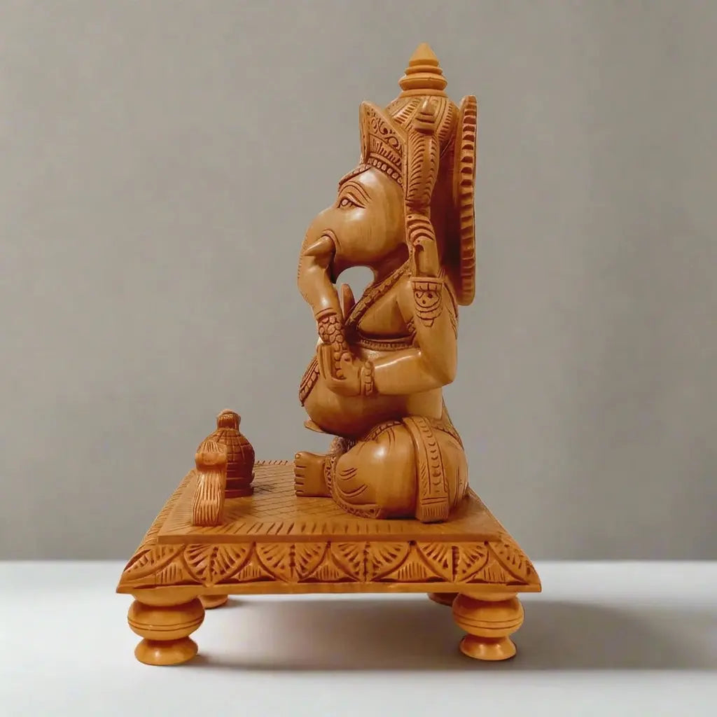 Side view of a wooden Ganesh idol with natural polish, showing the carved crown and patterned chowki legs