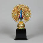 A handcrafted wooden dancing peacock memento intricately studded with shimmering stones on a polished base.