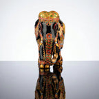 Front view of black wooden elephant showing a golden head covering, floral trunk decoration and white tusks