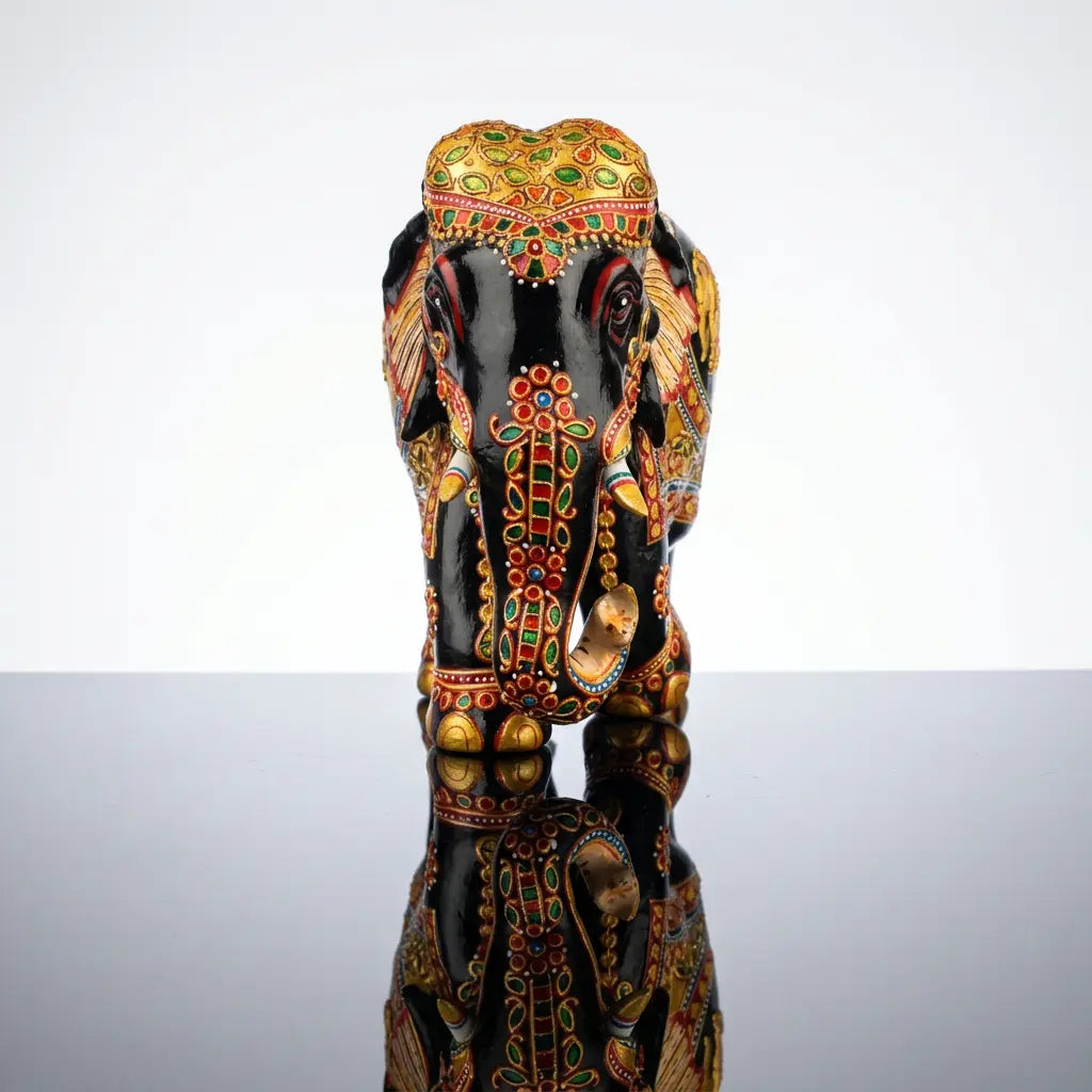 Front view of black wooden elephant showing a golden head covering, floral trunk decoration and white tusks