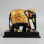 Side view of a black wooden elephant memento with gold floral painting and a downward trunk on a polished platform