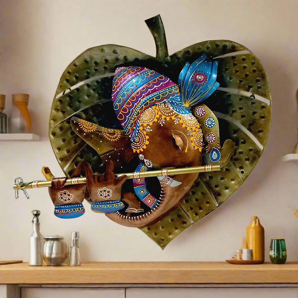 Decorative metal wall hanging of Ganesh on leaf, adorned with colorful hand painting for spiritual and aesthetic appeal.