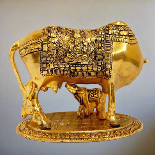 Metal Kamdhenu cow idol with calf drinking milk, adorned with bell and religious figures