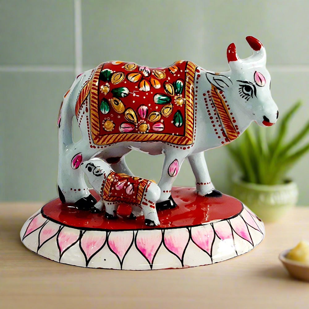 A beautiful metal cow and calf statue with intricate Meenakari painting, adorned with a red color.