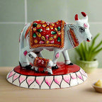 A beautiful metal cow and calf statue with intricate Meenakari painting, adorned with a red color.