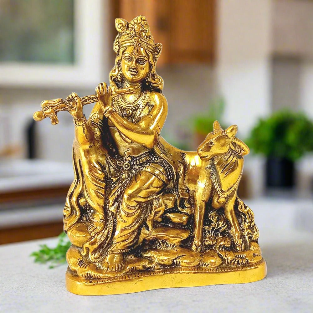 A metal Krishna idol sitting and playing the flute, with a cow's calf sitting nearby.