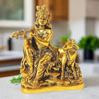 A metal Krishna idol sitting and playing the flute, with a cow's calf sitting nearby.
