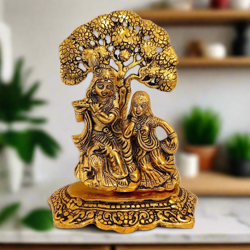 Metal Radha Krishna idol with golden oxidised polish, depicting Radha and Krishna sitting under a tree