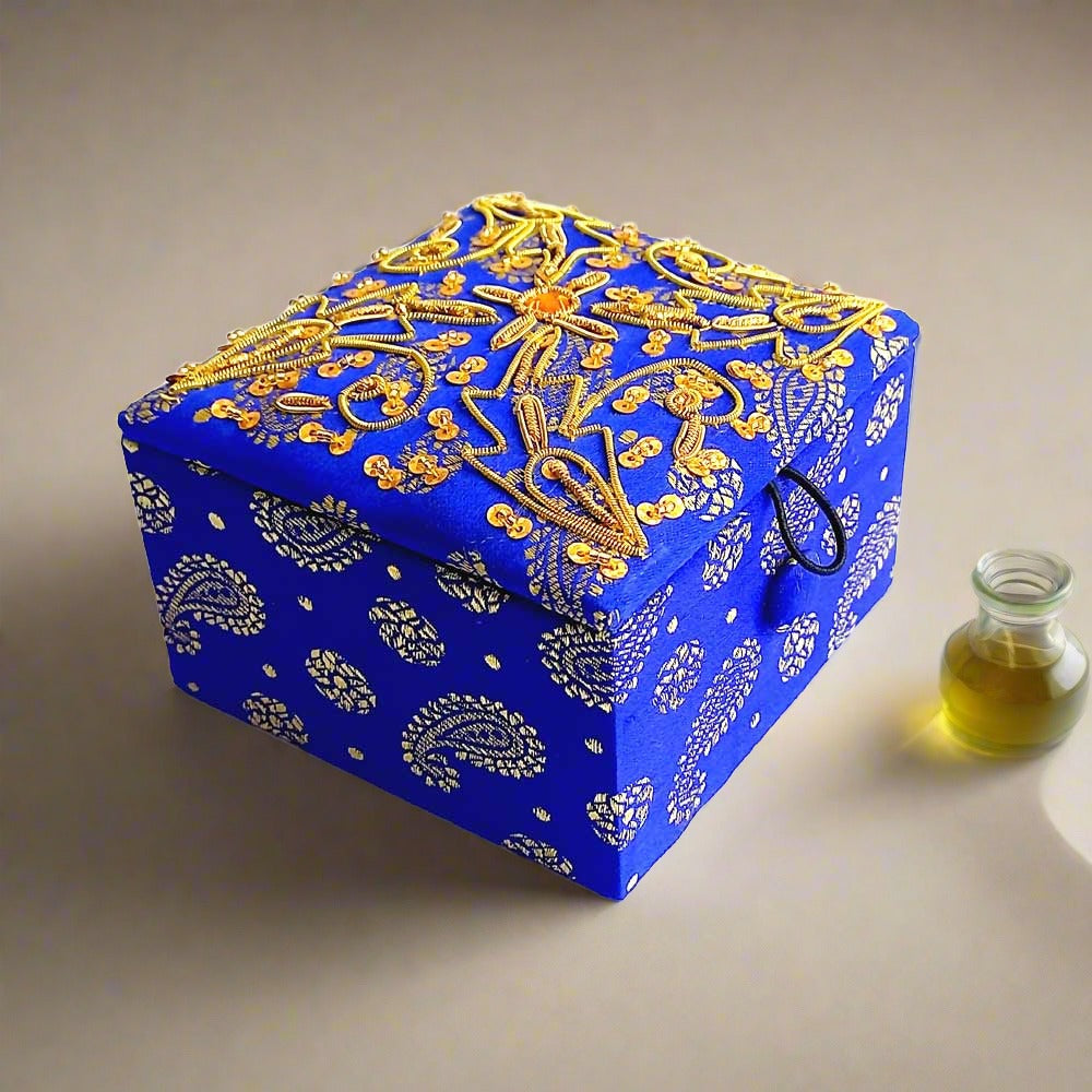 Small silk fabric box adorned with fine zardosi hand embroidery using golden wire and sequins, suitable for storing small jewelry.